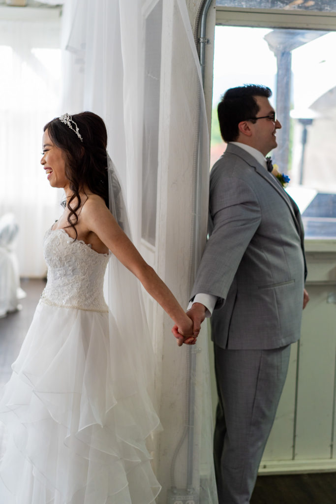 Alternative to a first look as groom and bride holding hands behind a window