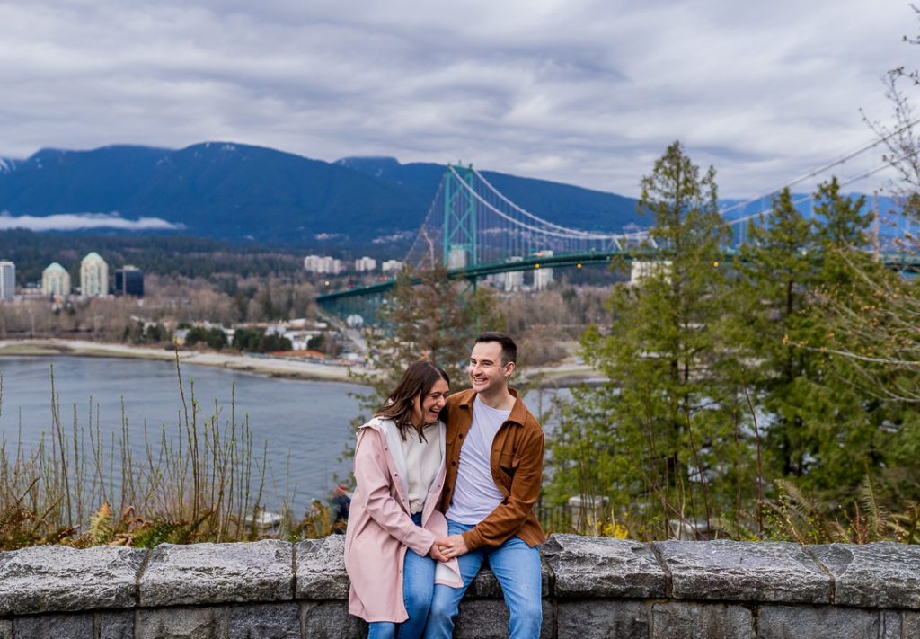 couple laughing in front of Lions Gate Bridge